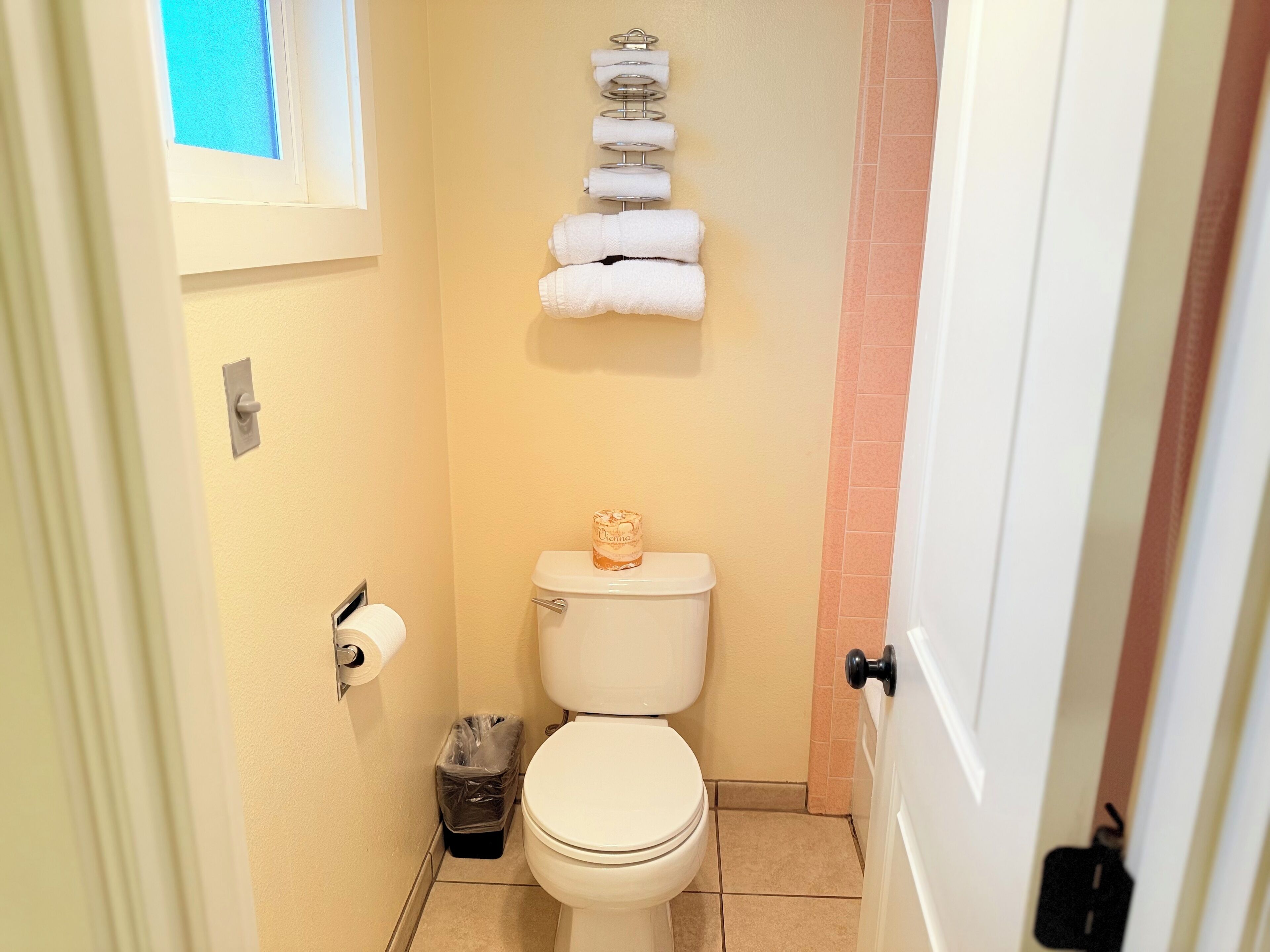 Un baño pequeño con inodoro, un cubo de basura y un toallero con varias toallas.