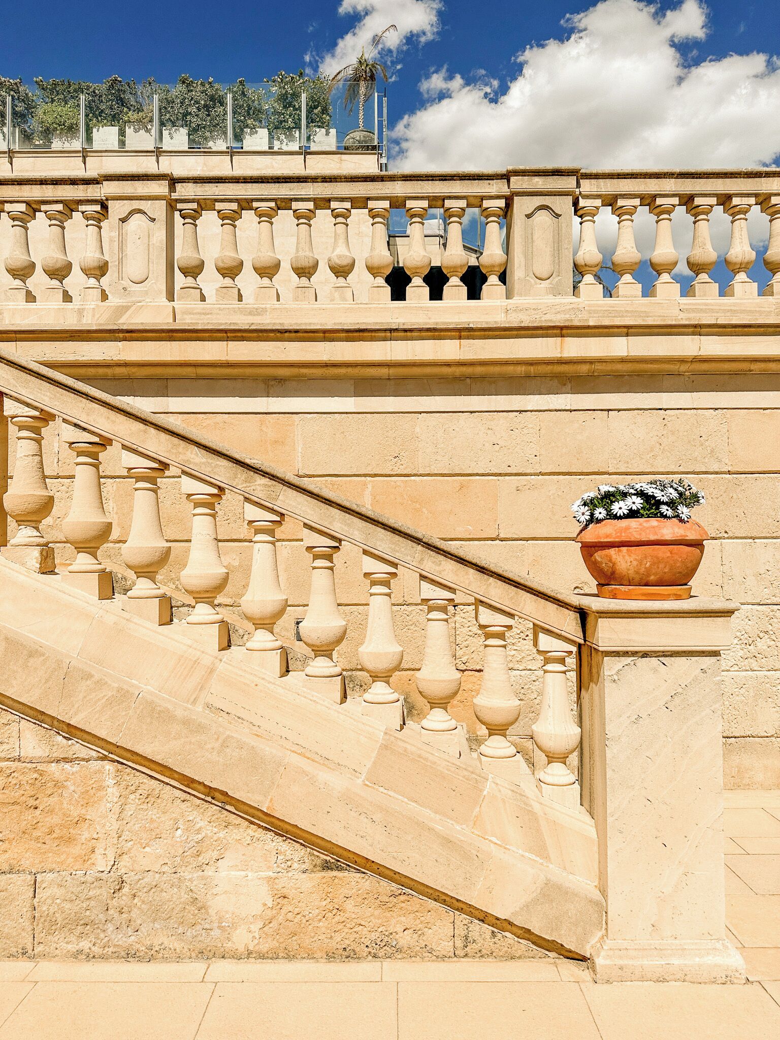 Una scala in pietra con balaustre, una vasca in terracotta con fiori e un cielo azzurro intenso.