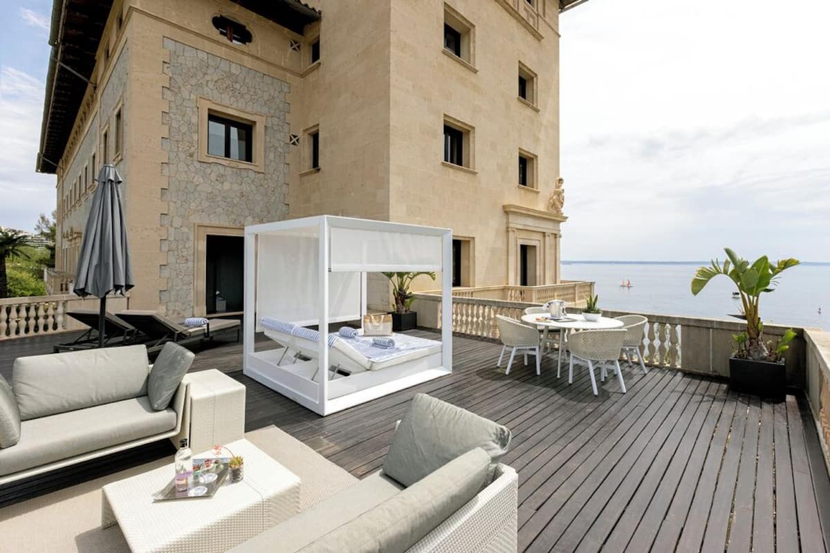 Ein Balkon mit einem Bett, einem Sofa und einem Esstisch.