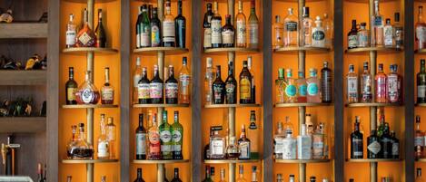 A bar with multiple shelves of bottles and glasses, and four bar stools in front.