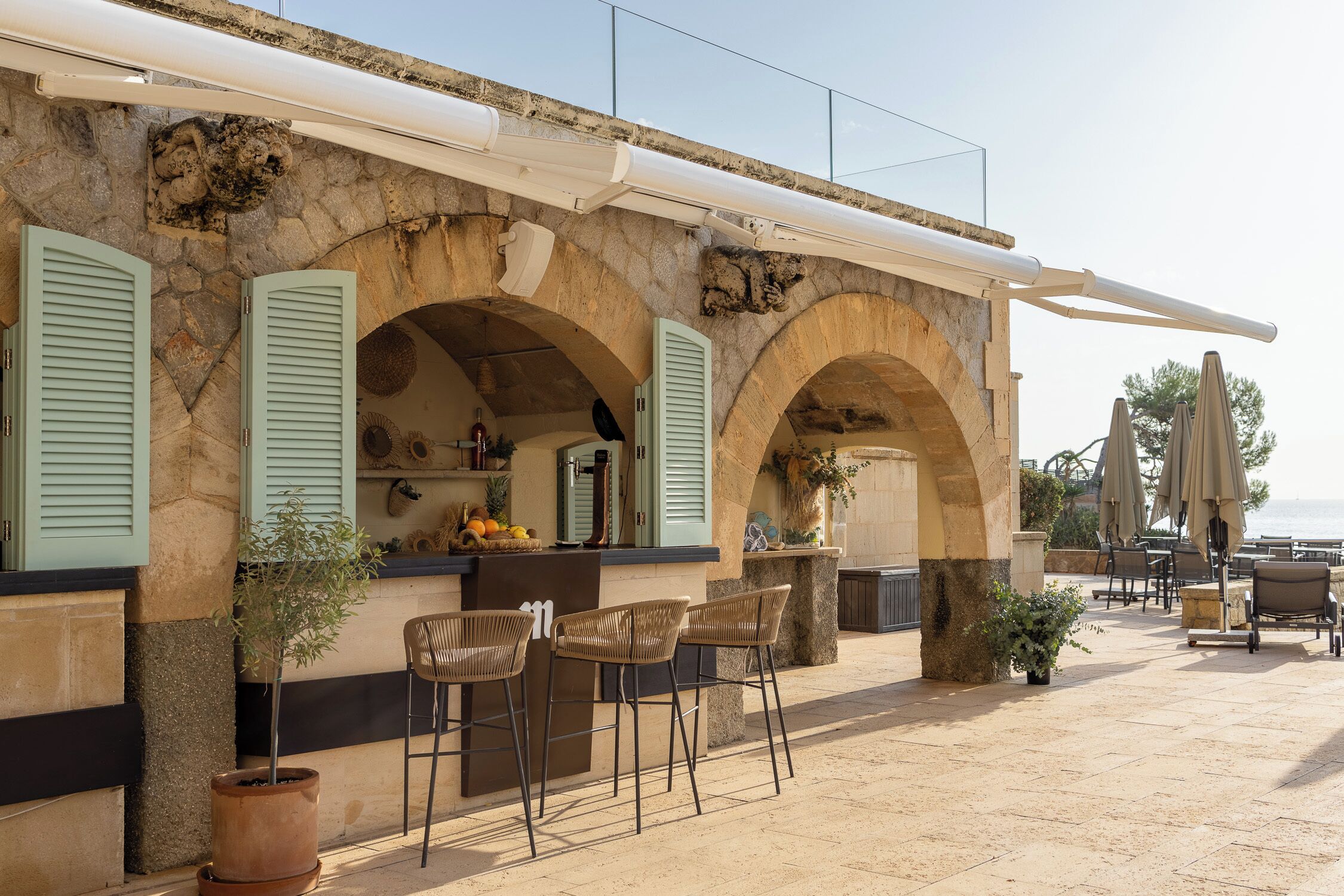 A stone building with a bar area, outdoor seating, and a view of the sea.