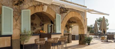 A stone building with a bar area, outdoor seating, and a view of the sea.