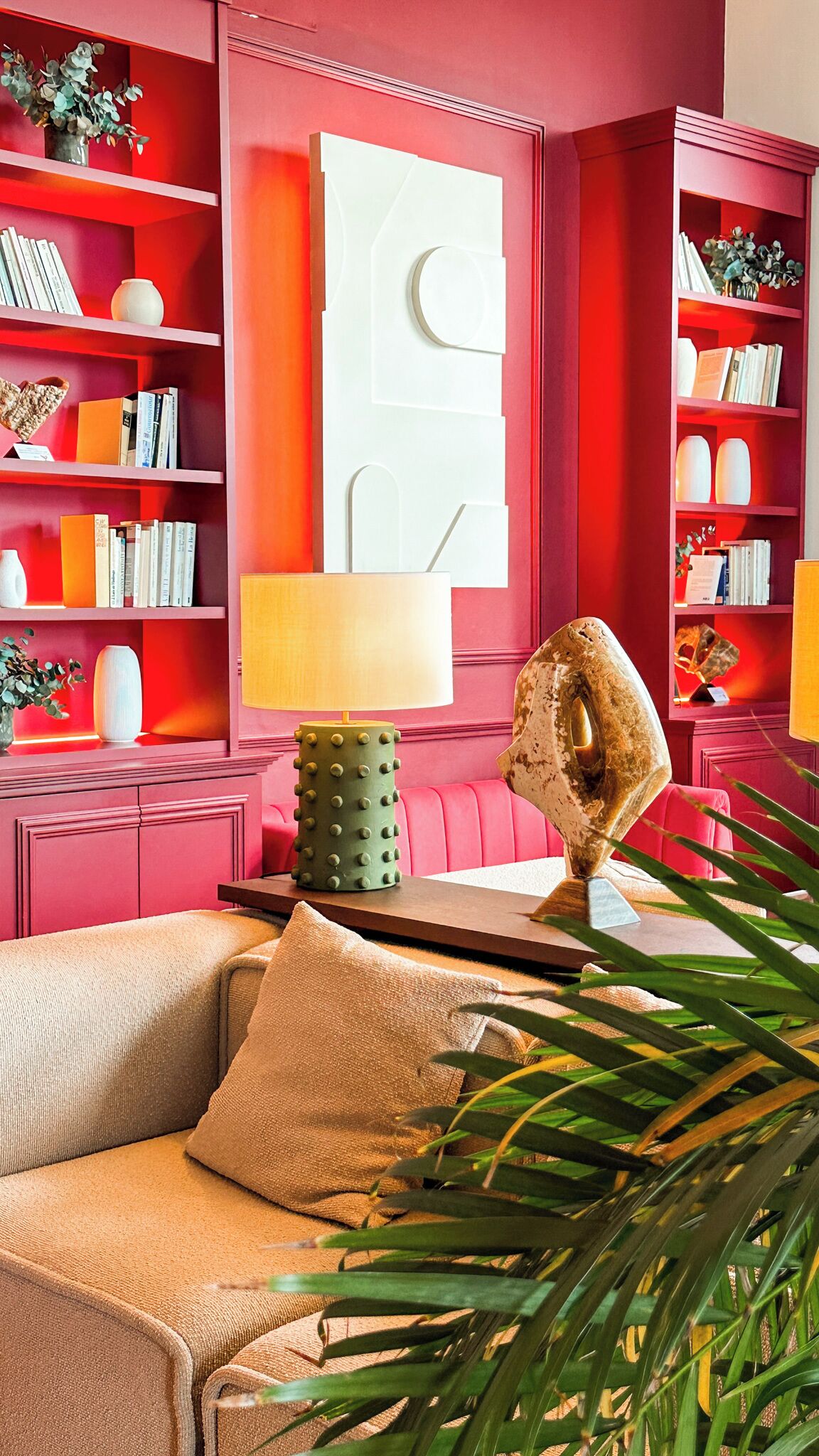 A modern living room with a beige sofa, a green lamp, and a large abstract sculpture.