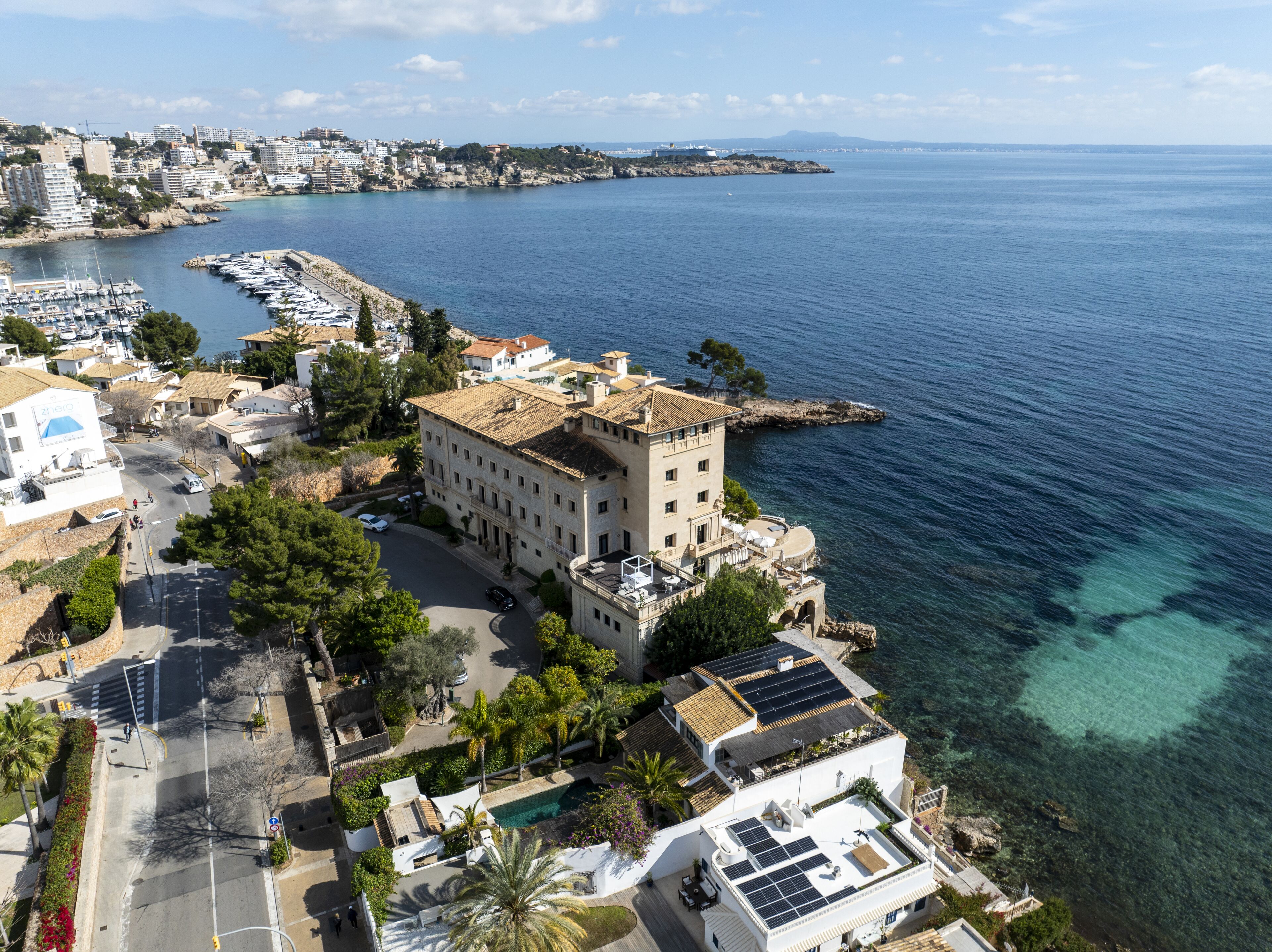 A coastal hotel with a large building, a marina, and clear blue waters.