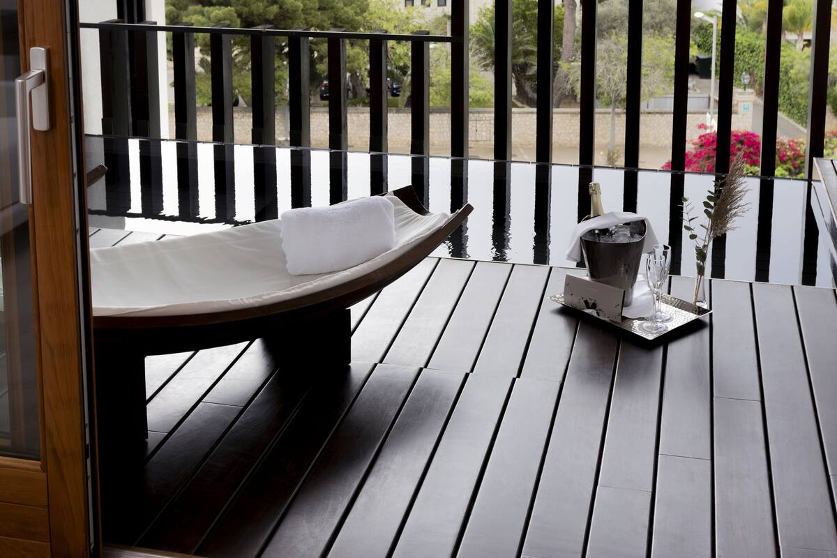 Ein Balkon mit Holzboden, einer Bank und einem kleinen Tisch mit einer Vase und einer Kerze.