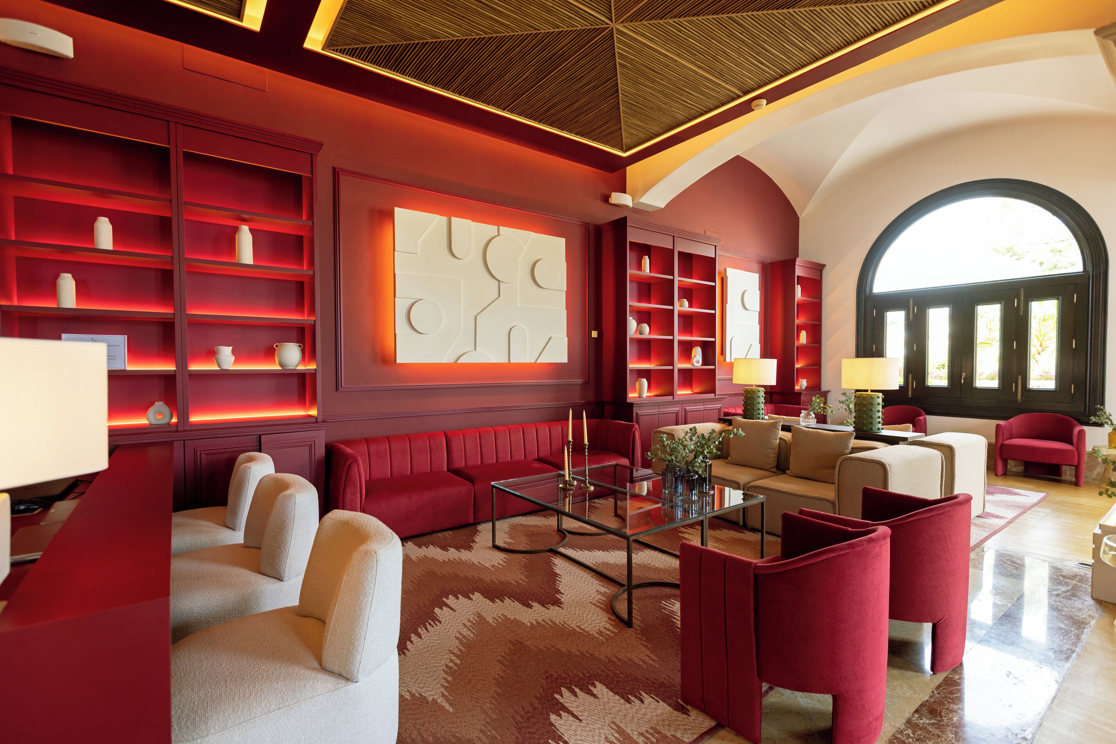 A spacious living area with red and beige furniture, a glass coffee table, and a large abstract wall art piece.