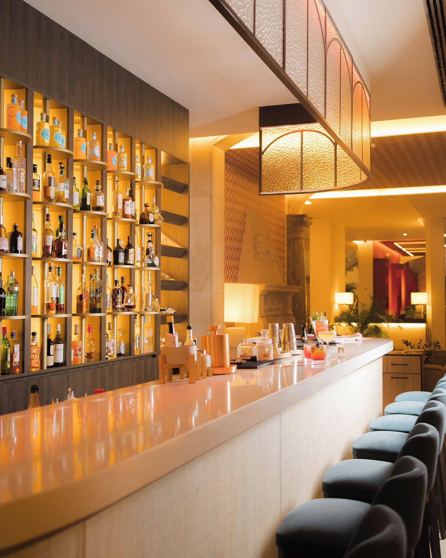 A bar area with shelves of liquor bottles, a counter with bar tools, and a seating area with cushioned chairs.