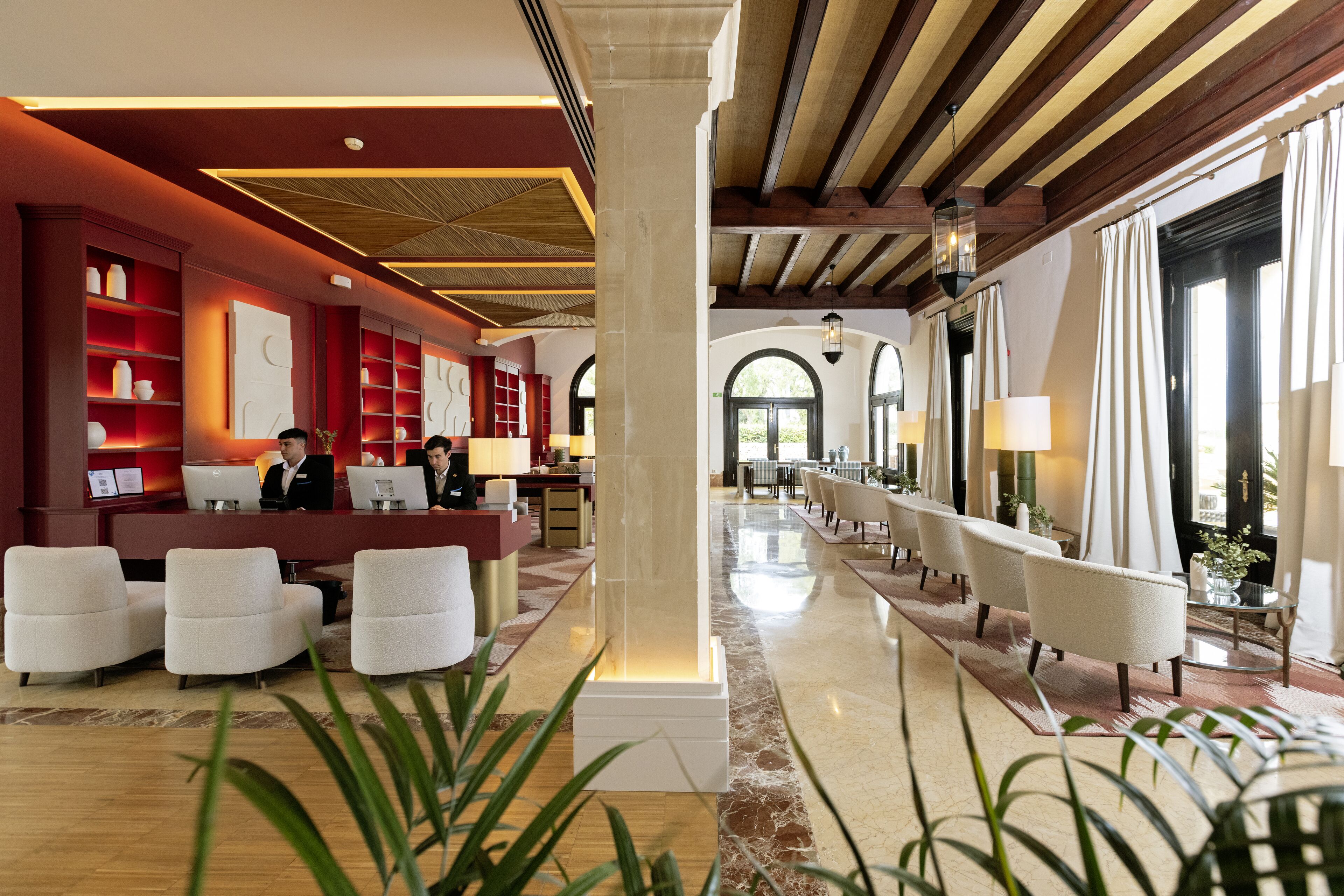 A hotel lobby with a reception desk, seating area, and large windows.