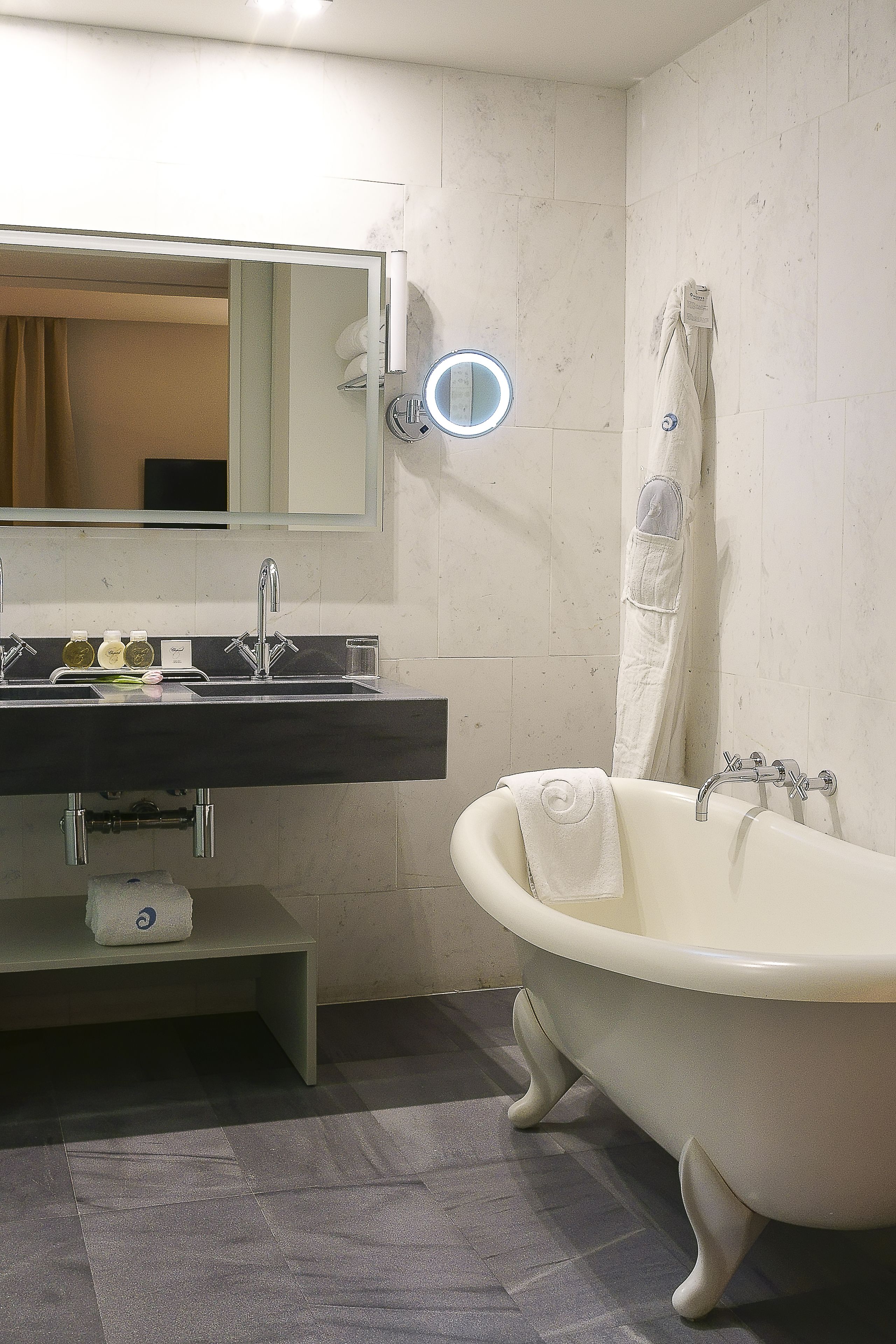 A bathroom with a freestanding bathtub, a vanity with a mirror and sink, and a towel hanging on the wall.