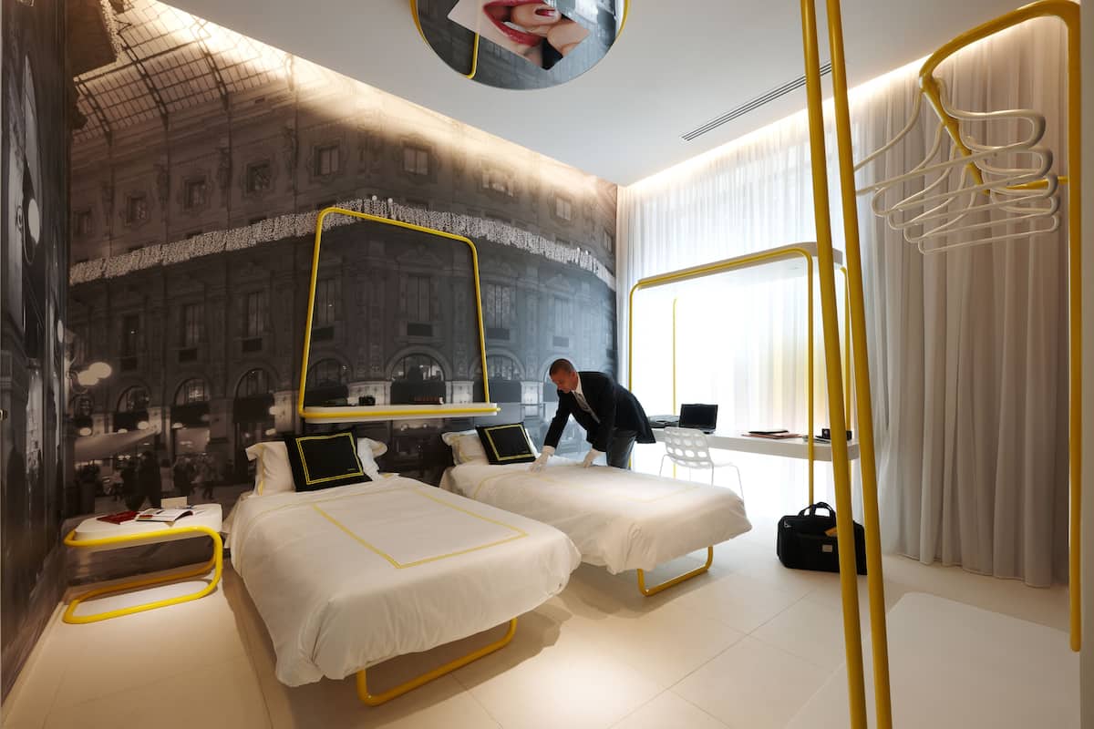 Camera d'albergo moderna con due letti, un grande specchio e vista sulla città attraverso la finestra.