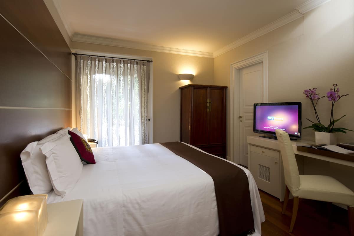 Una camera d'albergo con un letto, una scrivania con un computer, una sedia, un armadio e una finestra con tende.