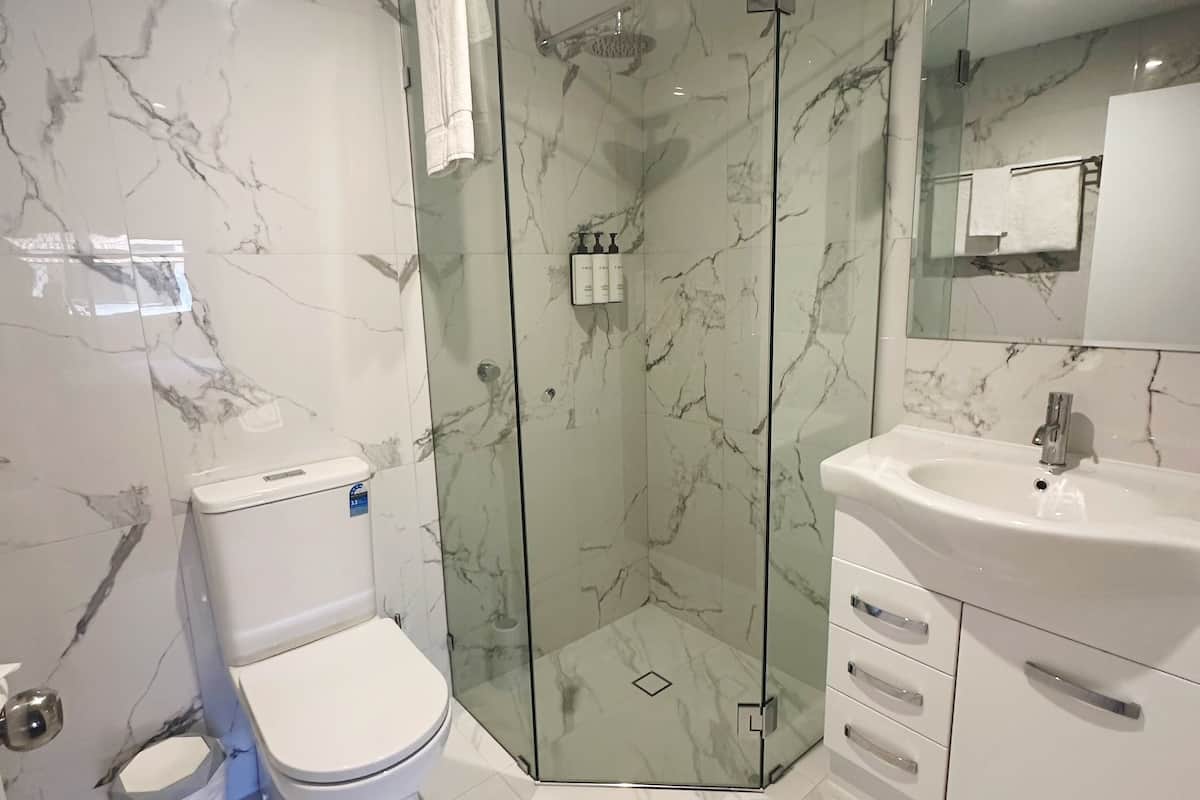 Ein modernes Badezimmer mit einer Duschkabine, einer Toilette und einem Waschbecken mit Spiegel darüber.