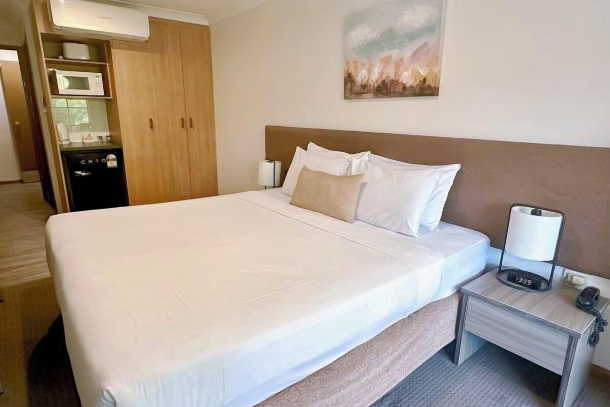A hotel room with a large bed, a bedside table with a lamp, a microwave, and a refrigerator.