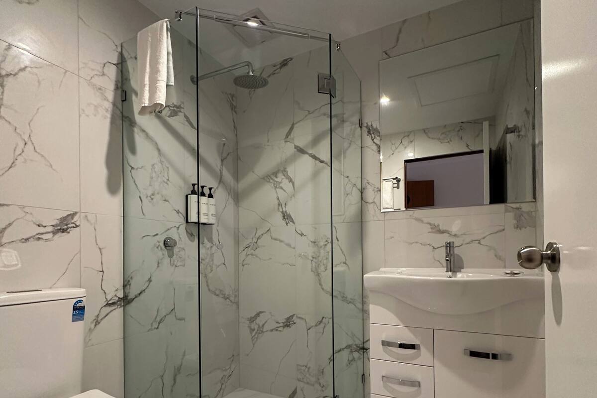 Ein modernes Badezimmer mit einer ein Glasfach umschlossenen Dusche, einer weißen Toilette und einem Waschbecken mit Spiegel darüber.
