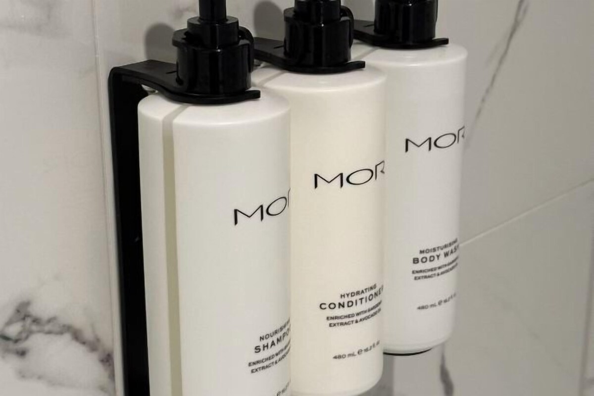Three bottles of MOR body wash on a white tiled wall.