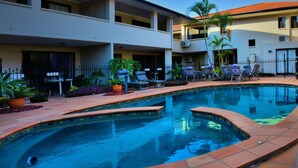 Una piscina con deck de baldosas, rodeada de sillas de descanso y plantas en macetas.