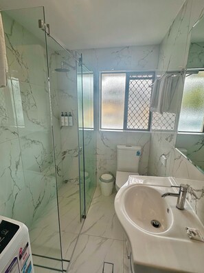 A bathroom with a glass-enclosed shower, a white sink, and a toilet. - Quest Ascot (Ascot)