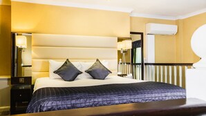 Quarto de hotel com uma cama grande, mesas de cabeceira, um espelho e um aparelho de ar condicionado.
