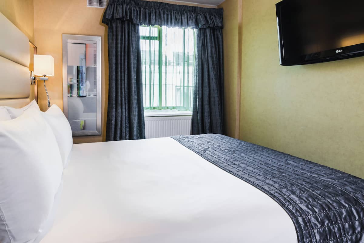 Une chambre d’hôtel avec un grand lit, un téléviseur à écran plat, une fenêtre avec des rideaux et un miroir.