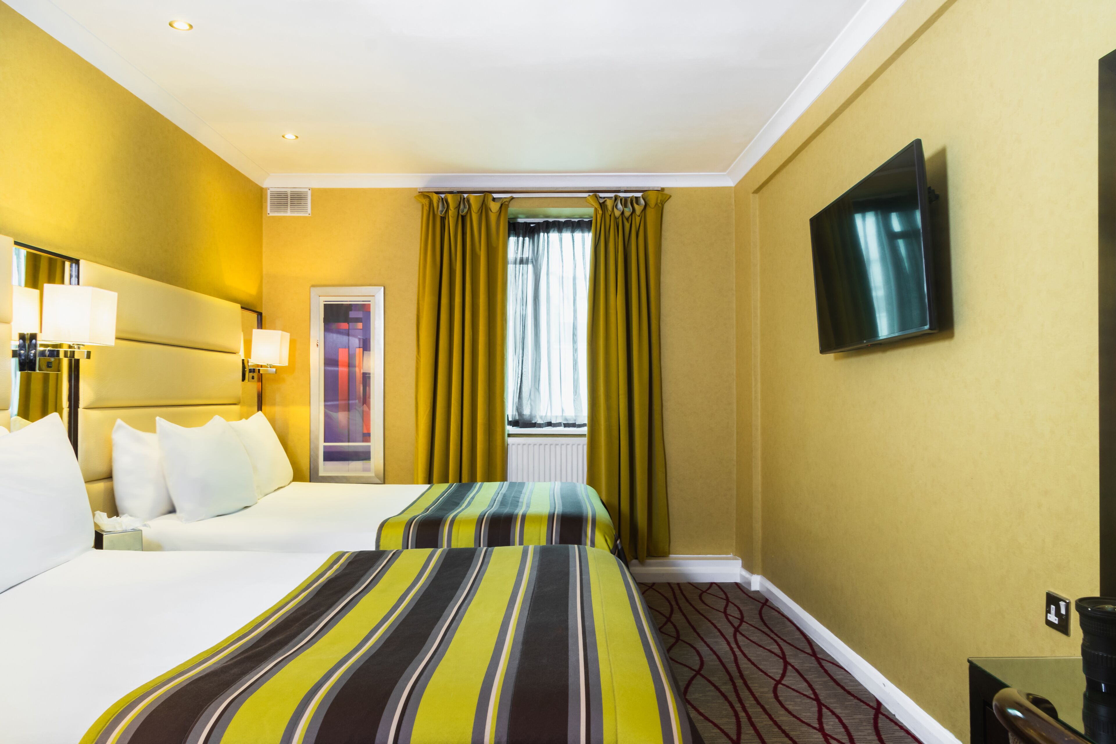A hotel room with two beds, a television, and a window with curtains.
