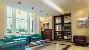 Um hall moderno com sofás verde-água, uma mesa de centro com revistas e amplas janelas com luz natural.