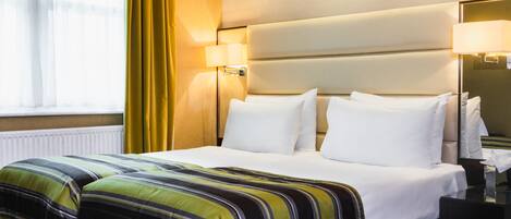 A hotel room with a bed, a nightstand, a lamp, and a window with curtains.