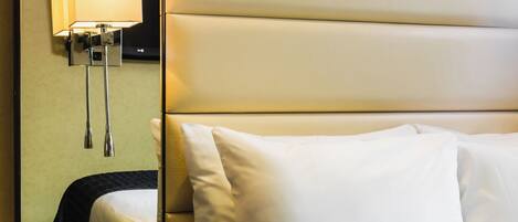 A hotel room with a bed, a nightstand, a mirror, and a wall-mounted lamp.
