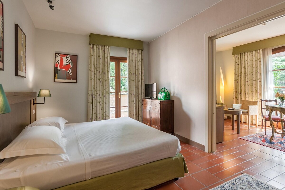 Habitación de hotel con cama, escritorio con televisor y zona de comedor con mesa y sillas.