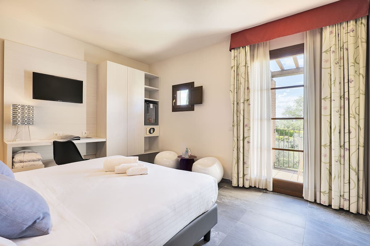 A hotel room with a bed, a desk, a TV, and a balcony with curtains.