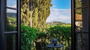 Un balcon avec une table et des chaises, donnant sur un paysage verdoyant et luxuriant et sur une ville située au loin.