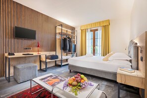 A modern hotel room with a bed, desk, TV, and a fruit bowl on the table. - Villa San Paolo (San Gimignano)