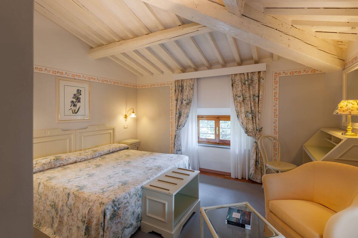 A bedroom with a bed, a chair, a small table, and a window with curtains.