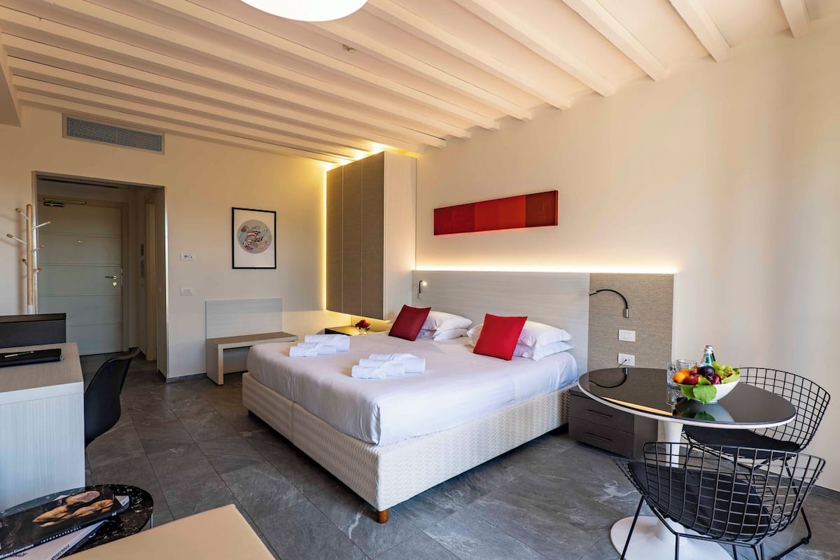 A modern hotel room with a large bed, a desk, a dining table, and a chair.