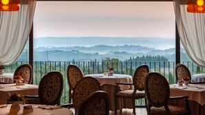Un espace repas avec des tables dressées pour quatre personnes, chacune agrémentée d’une nappe blanche et d’une composition florale, offrant une vue imprenable sur un paysage montagneux.