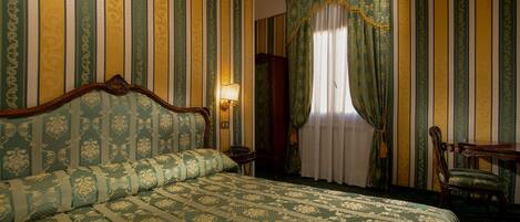 A room with a large bed, a wooden nightstand, a desk, and a chair.