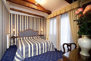 Ein Zimmer mit einem Bett, einem Sessel, einem Tisch und einer Vase mit Blumen.