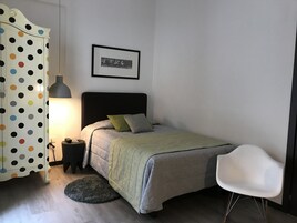 Una camera da letto con un letto, una sedia, una lampada, un quadro appeso e un armadio a pois.