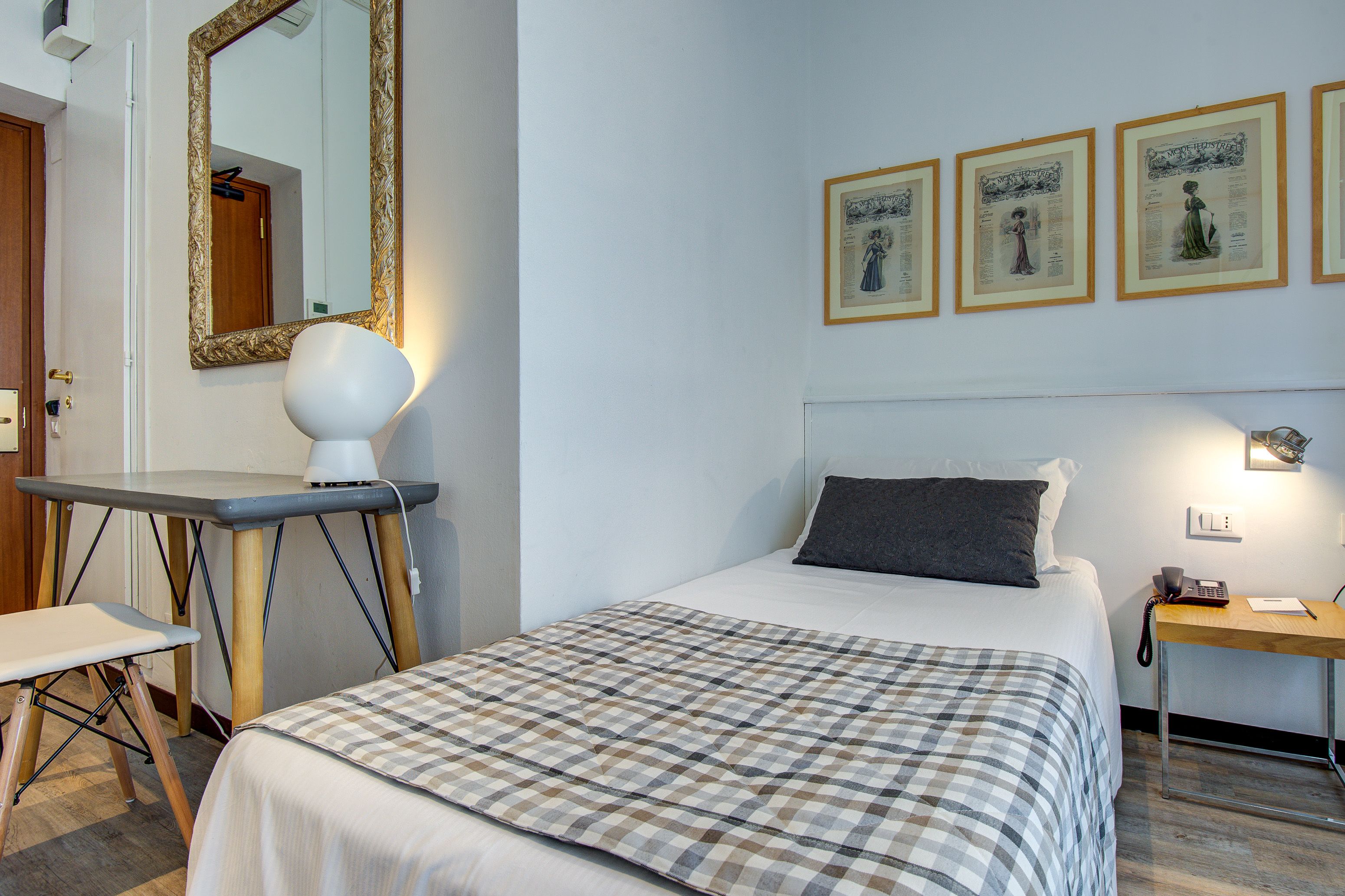 A neatly arranged hotel room with a bed, bedside table, lamp, and a wall-mounted mirror.