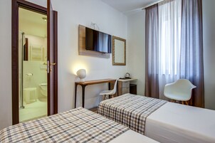 Een hotelkamer met twee bedden, een bureau, een stoel, een spiegel en een raam met gordijnen.