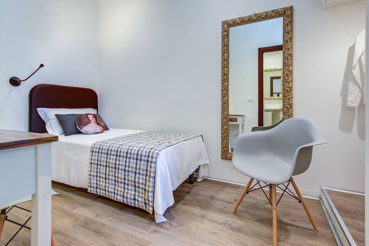 A bedroom with a bed, a chair, a mirror, and a dresser.