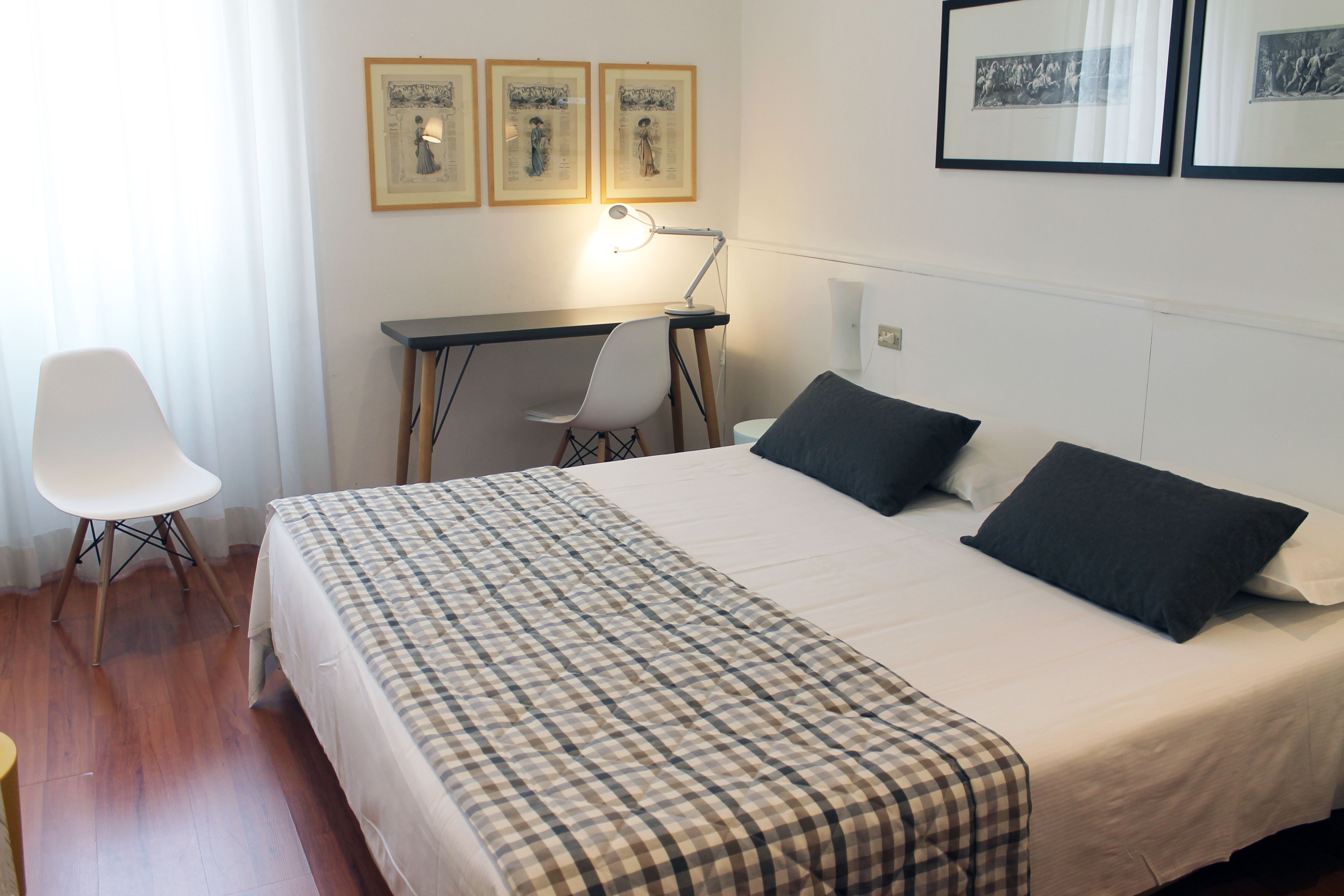 A hotel room with a bed, a desk, and a chair. There are three framed pictures on the wall.