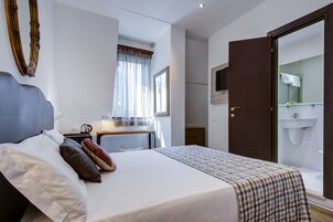 A hotel room with a bed, a desk, a mirror, and a bathroom visible through an open door.