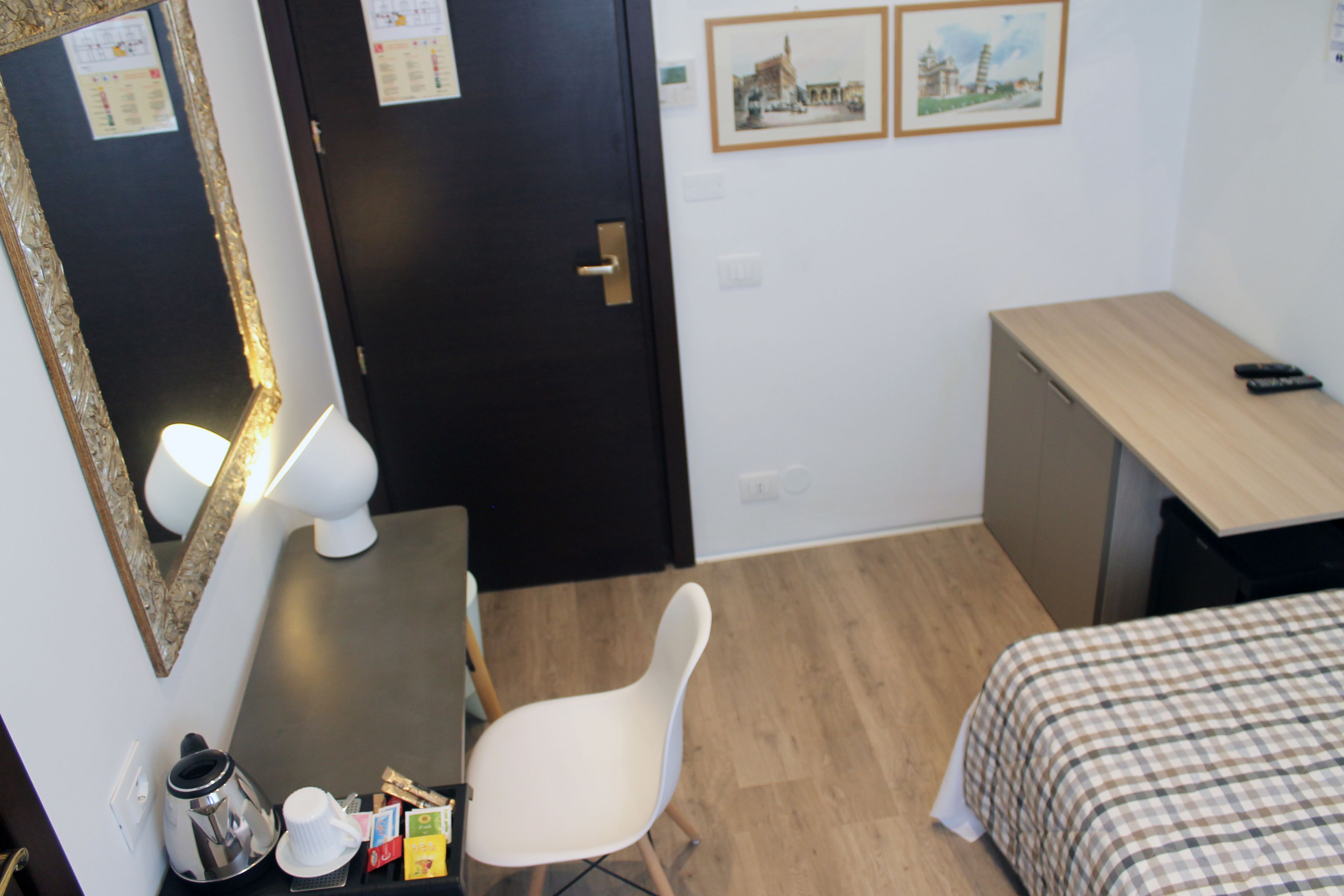 Una habitación pequeña y ordenada con una cama, un escritorio, una silla y un espejo.