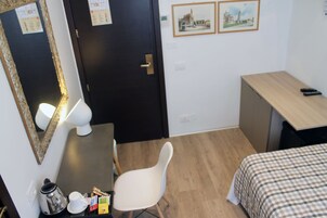 Pieni, siististi järjestetty huone, jossa on sänky, työpöytä, tuoli ja peili.