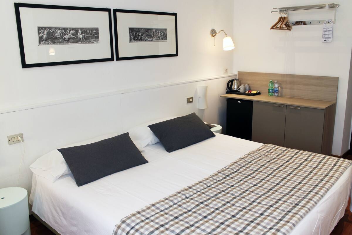 A neatly made bed with a plaid bedspread, a bedside table with a lamp, and two framed pictures on the wall.