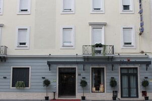 Ένα κτίριο με πολλά παράθυρα, μια πόρτα και γλάστρες με φυτά.