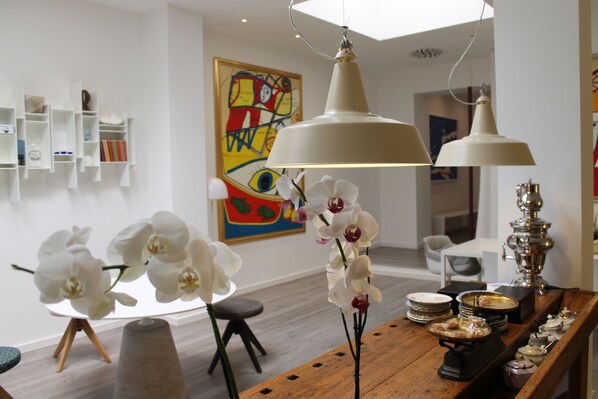 A modern dining area with white orchids, a wooden table, and a colorful abstract painting on the wall.