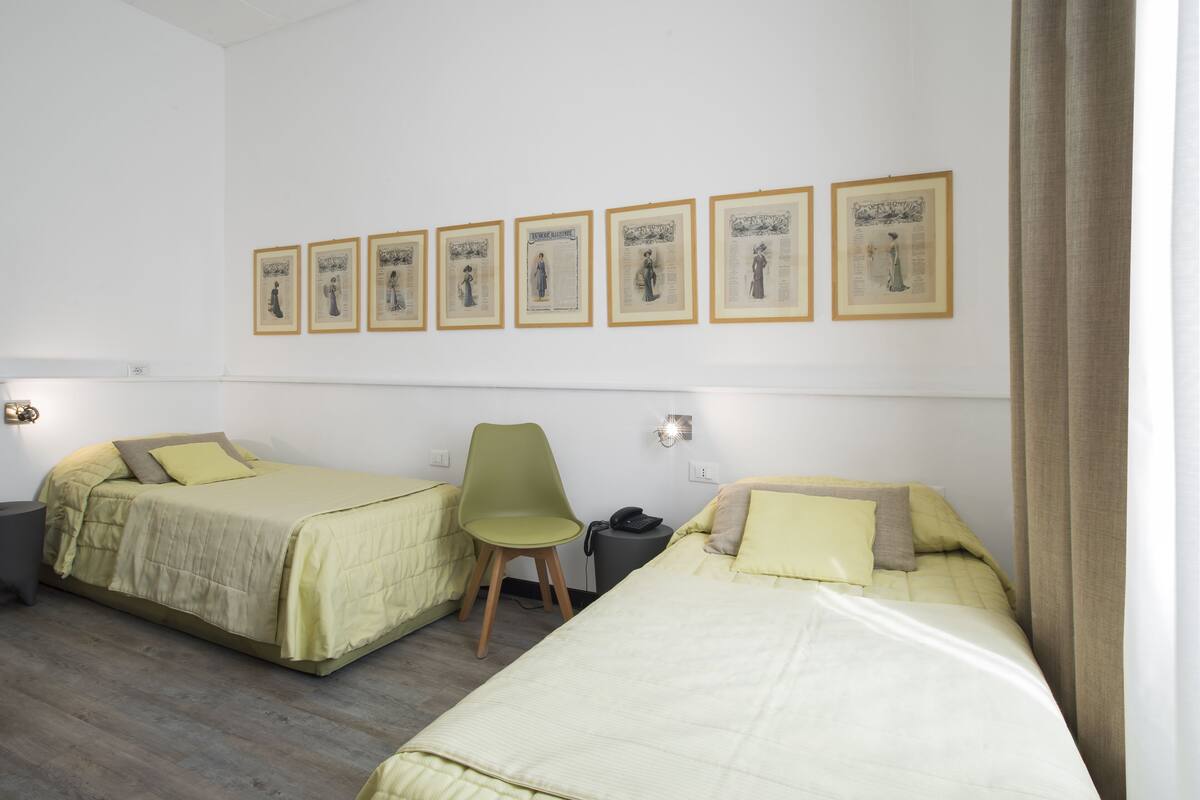 A hotel room with two beds, a chair, a desk, and framed pictures on the wall.