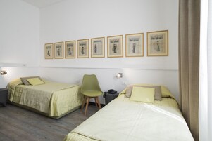 Ein Hotelzimmer mit zwei Betten, einem Sessel, einem Schreibtisch und gerahmten Bildern an der Wand.