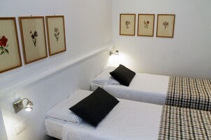 Una camera d'albergo con due letti singoli, biancheria da letto bianca, cuscini neri, una coperta a quadri e un quadro floreale incorniciato sulla parete.